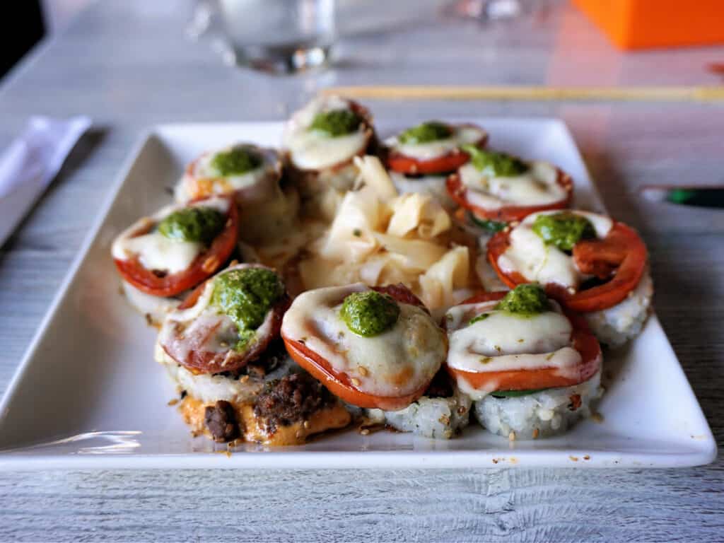 Sushi-style burger bites topped with tomato, melted cheese, and pesto.
