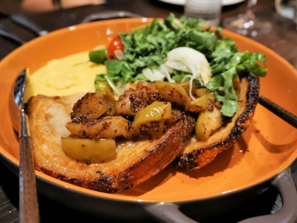 Pork chops topped with cooked apples and served with toast, eggs, and greens.