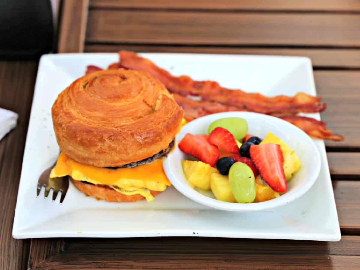 Croissanwich, fruit, and bacon on a plate.