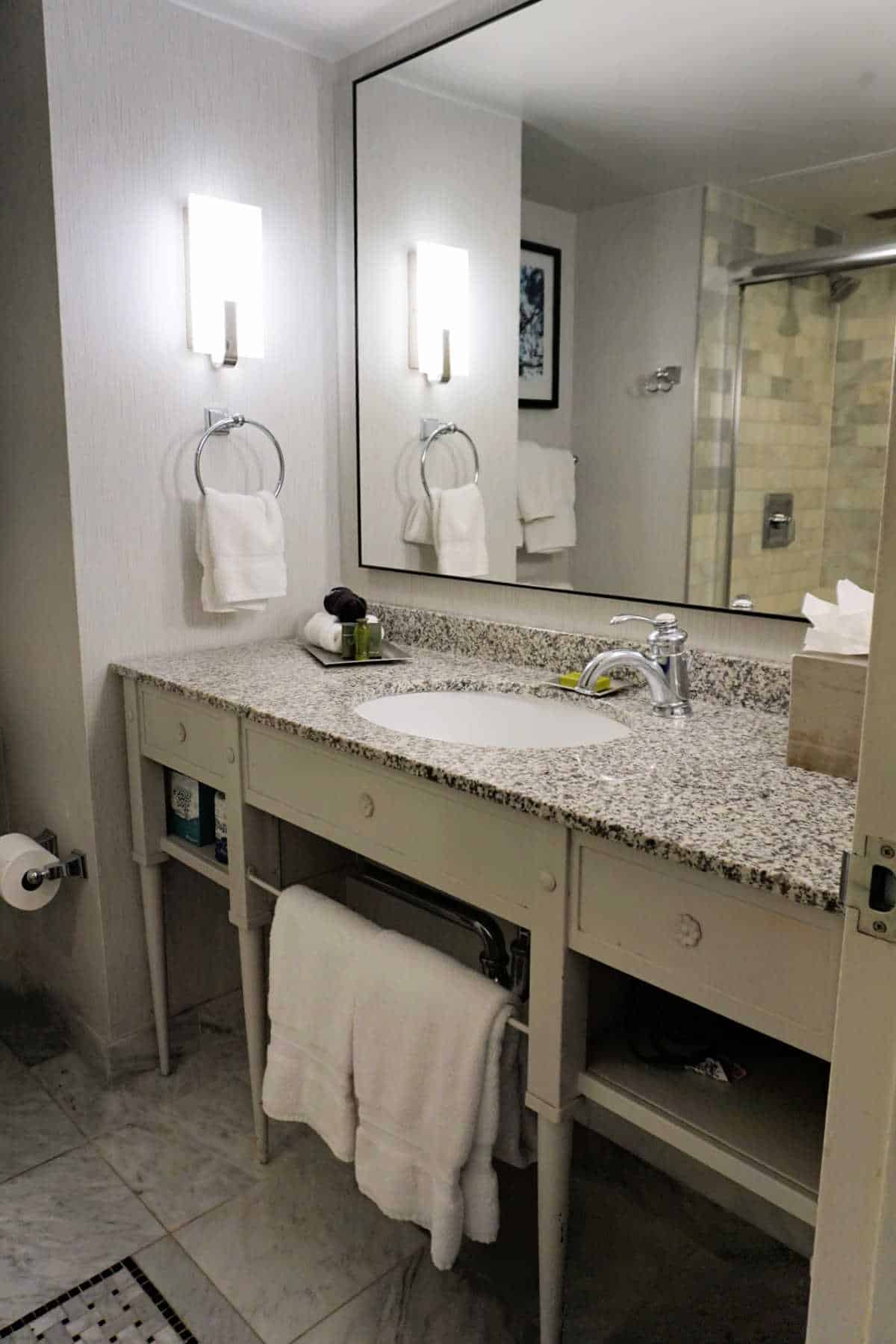 Modern hotel bathroom at The DeSoto Savannah with glass-enclosed shower and granite vanity.