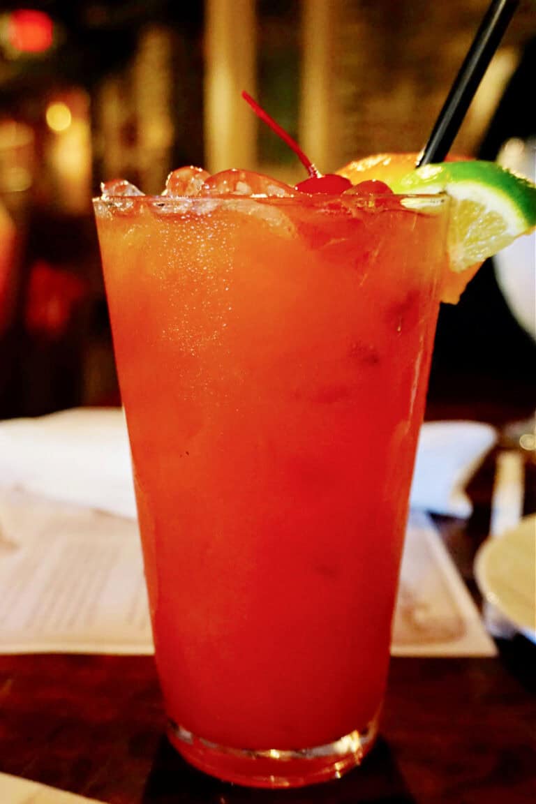 Cocktail in a large glass garnished with lime and orange wedges.