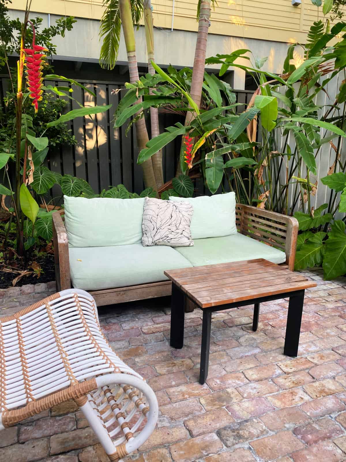 Green love seat and rattan chair on a brick-paved patio.