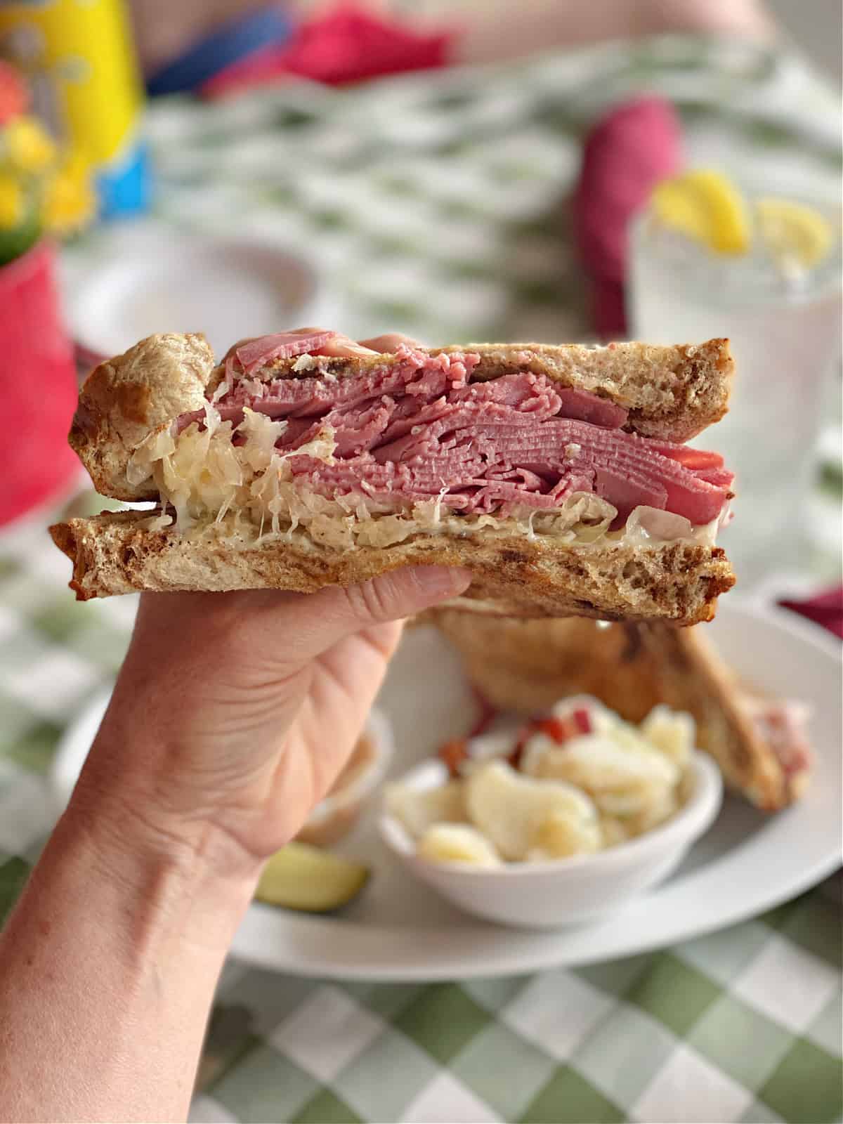 Hand holding a reuben sandwich with corned beef and sauerkraut.