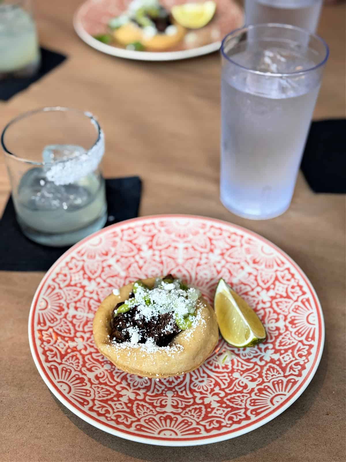 Piece of fry bread topped with beef and served with a lime wedge.