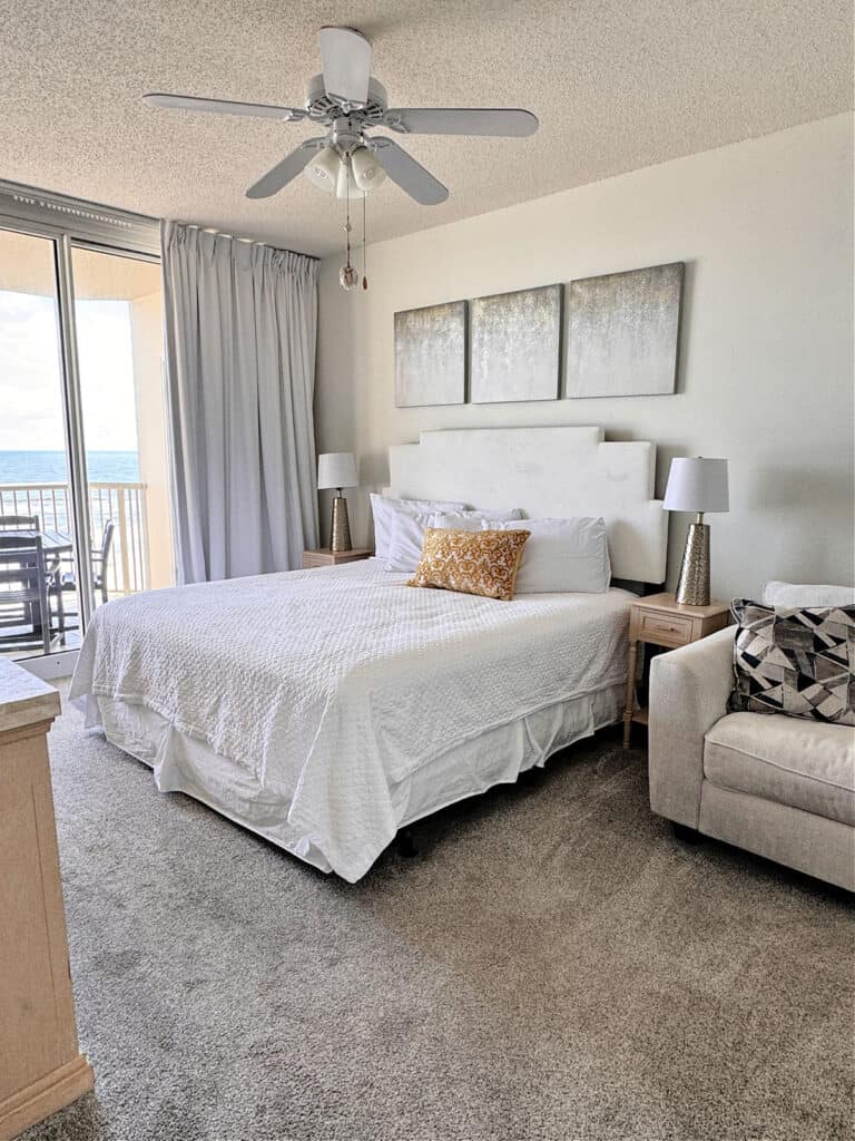 King size bed with white linens in a room with a door to a balcony with views of the ocean.