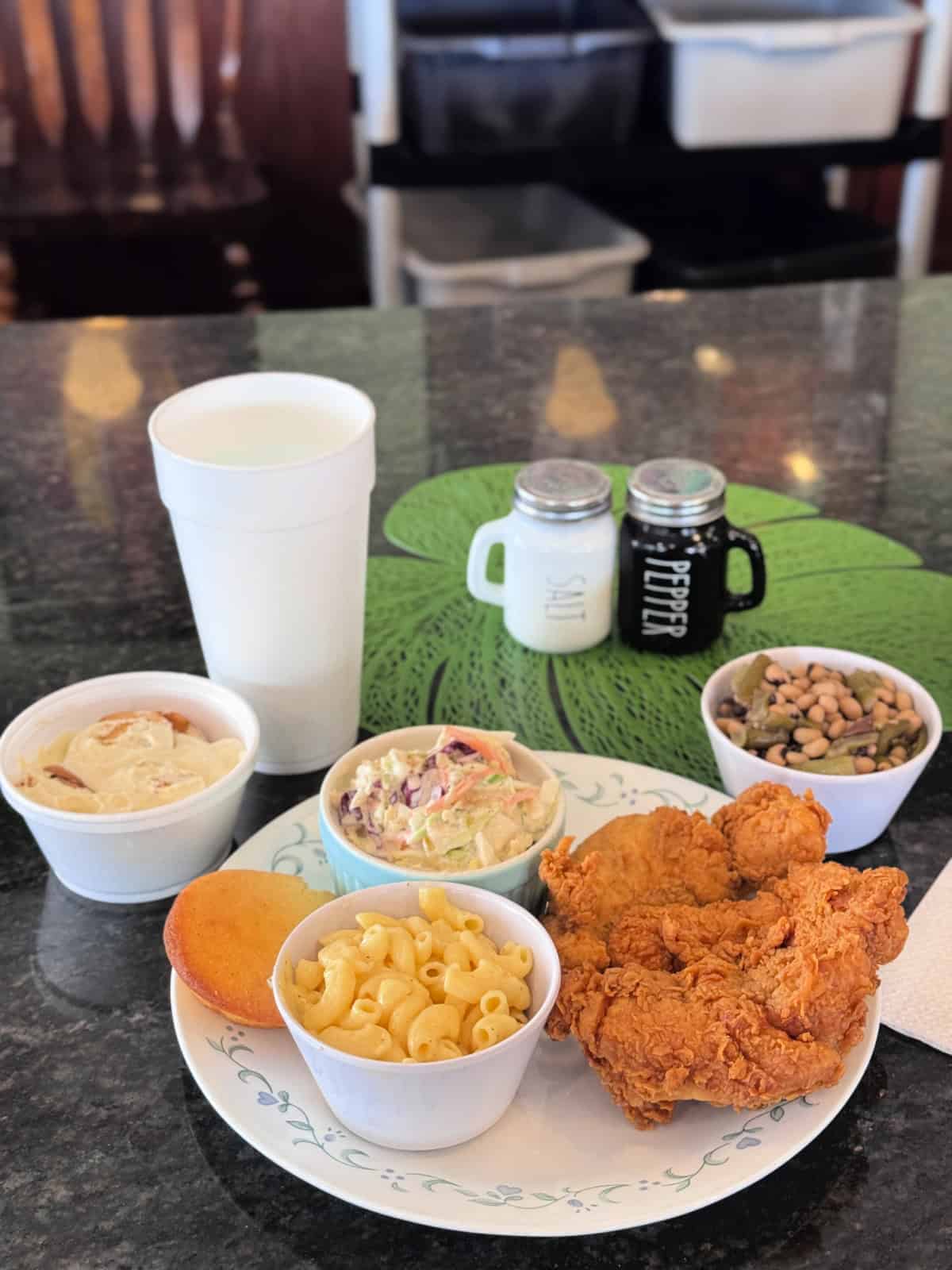 Three fried chicken fingers, macaroni and cheese, coleslaw, peas, banana pudding, and a cup of water.