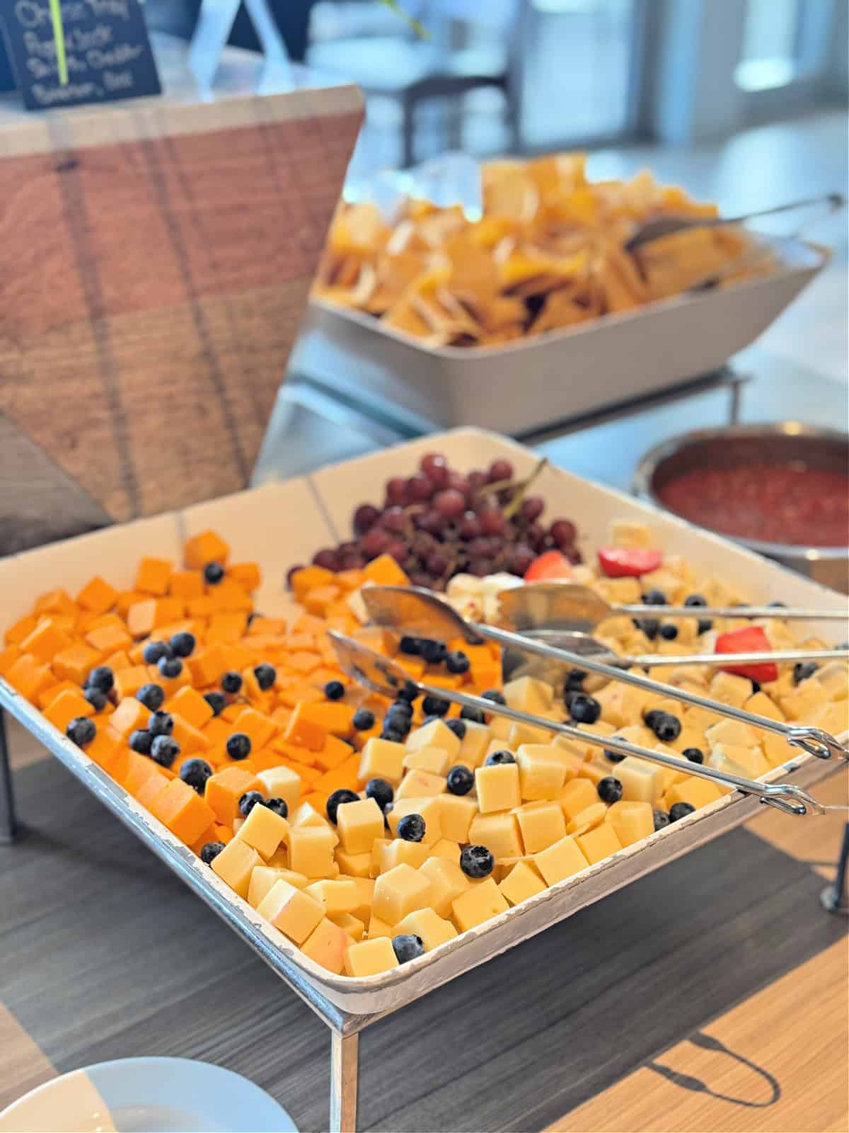 Platter of three types of cheese, strawberries, blueberries, and grapes.