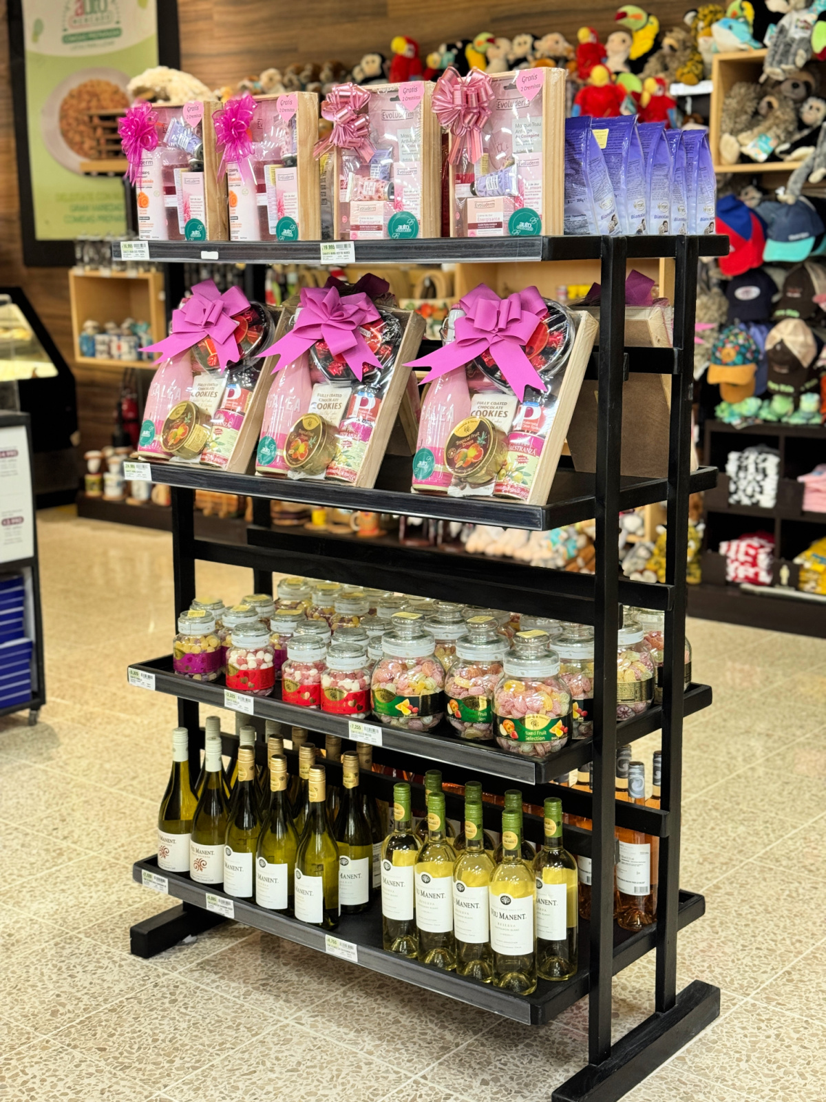A store display inside Auto Mercado showcasing gift baskets with pink bows, jars of assorted candies, and shelves of white and rosé wine bottles.