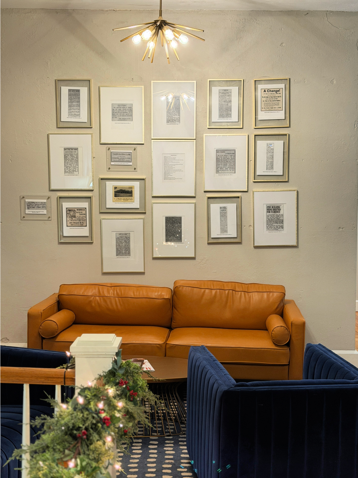 Lobby seating area at The Stricklin Hotel in Florence, Alabama, with leather sofa, velvet chairs, framed historic prints, and modern chandelier lighting.