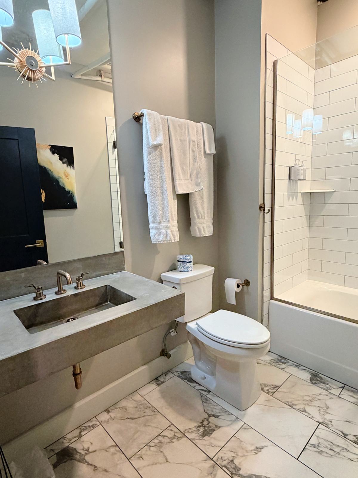 Modern bathroom at The Stricklin Hotel in Florence, Alabama, featuring a concrete vanity sink, marble-pattern tile flooring, toilet, and glass-enclosed shower.