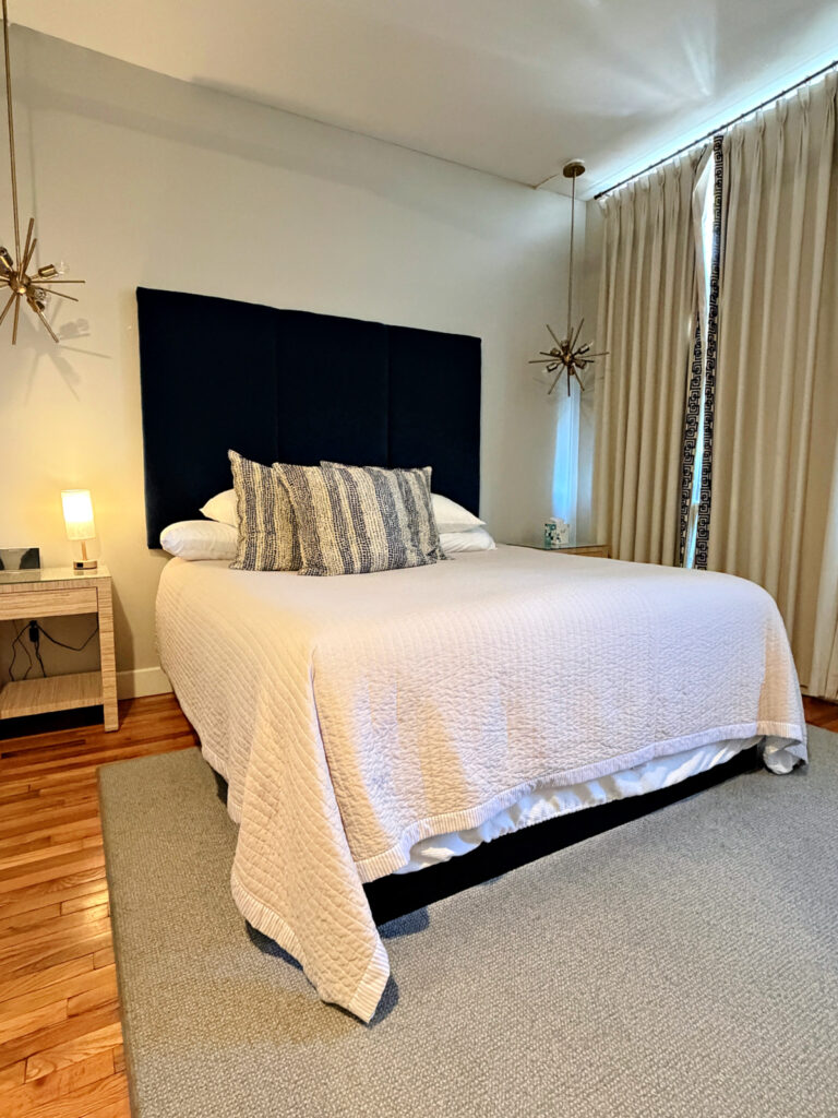 Modern guest room at The Stricklin Hotel in Florence, Alabama, with a king-size bed, navy upholstered headboard, white bedding, hardwood floors, and contemporary lighting.