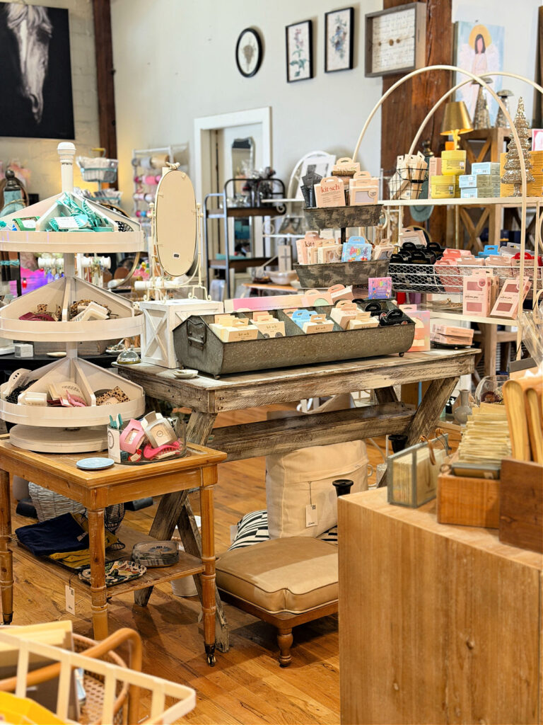 Boutique shopping area near The Stricklin Hotel in Florence, Alabama, featuring curated gifts, accessories, beauty items, and home decor displayed on rustic tables.