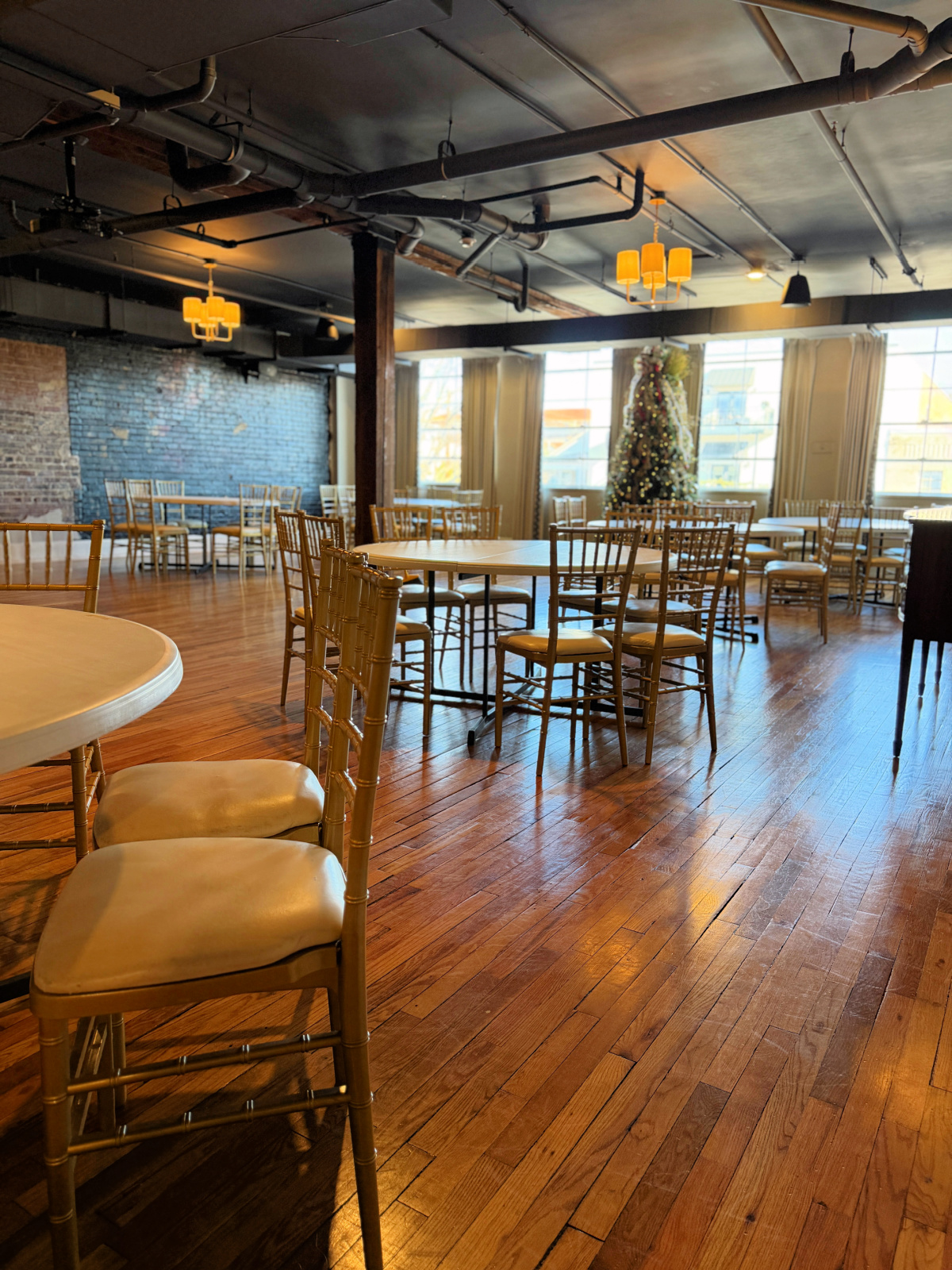 Communal lounge space at The Stricklin Hotel in Florence, Alabama, with long dining tables, bar seating, hardwood floors, large windows, and holiday decor.