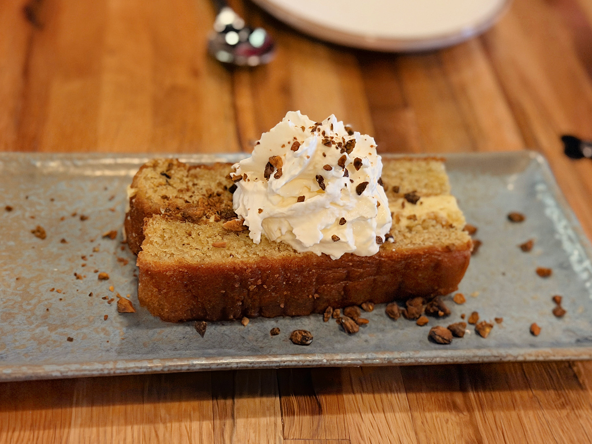 Slice of pistachio cake topped with whipped cream and toasted crumbs on a rectangular plate at Fig & Ash in Pittsburgh.