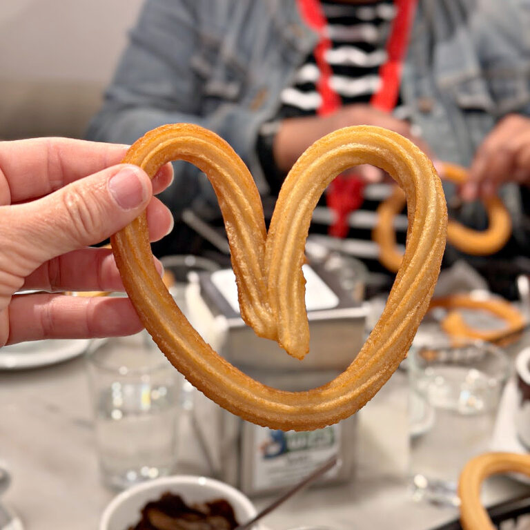 Heart shaped churro in front of a cup of Spanish hot chocolate.