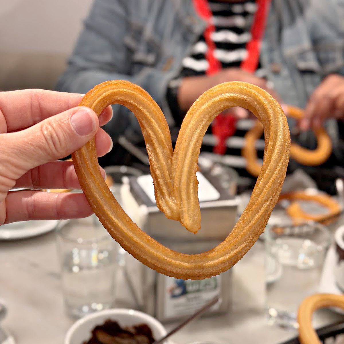 Heart shaped churro in front of a cup of Spanish hot chocolate.