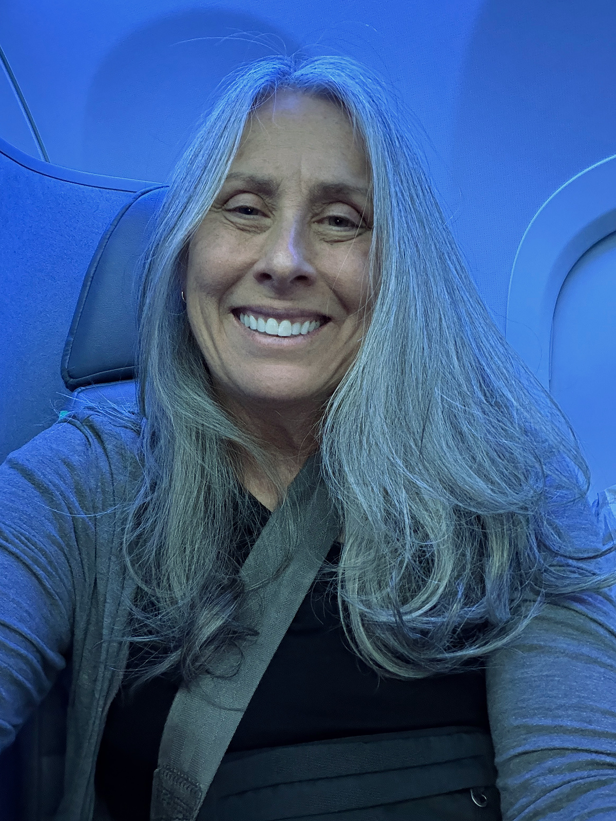 Passenger smiling in a JetBlue Mint private suite seat with blue mood lighting and seatbelt fastened before takeoff.