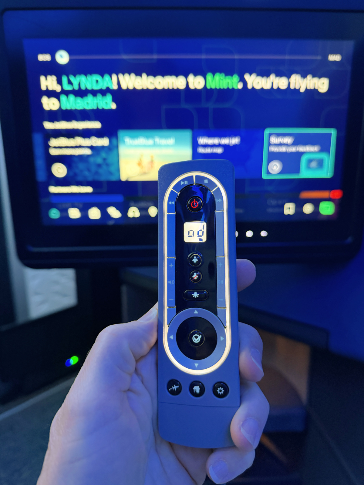 etBlue Mint handheld remote control in front of a personalized in-flight entertainment screen welcoming the passenger aboard.