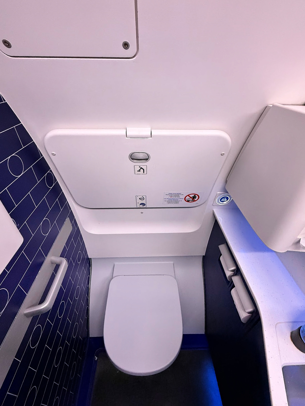JetBlue Mint aircraft lavatory with toilet, fold-down changing table, storage compartments, and blue accent wall.