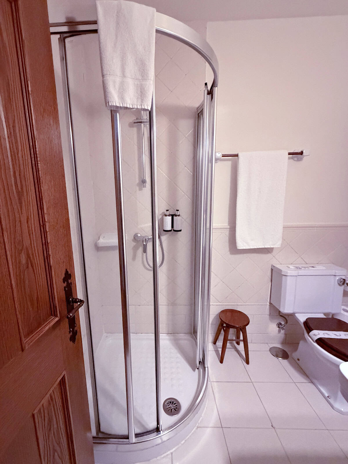 Bathroom with curved glass shower, white tile walls, and traditional wood accents at Hotel Airas Nunes in Santiago de Compostela.