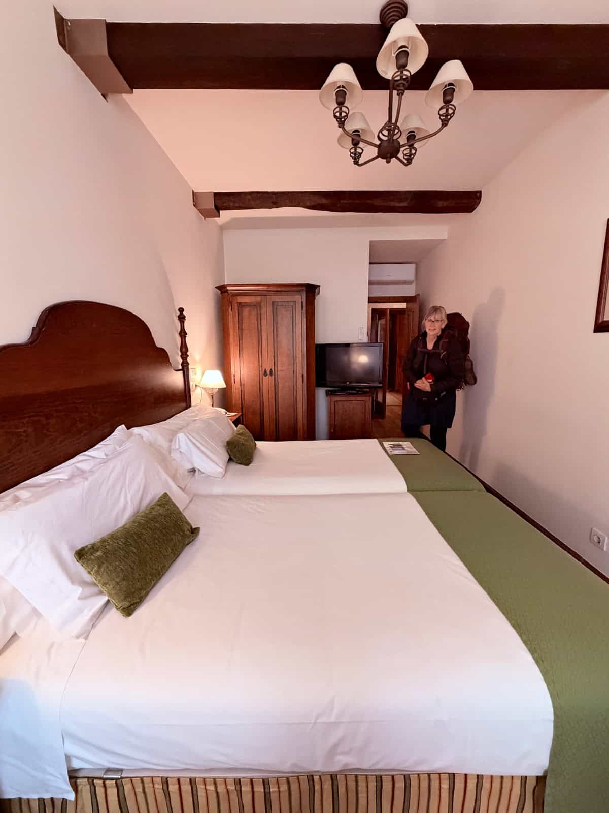 Guest room at Hotel Airas Nunes featuring twin beds, exposed wooden beams, antique furnishings, and a pilgrim arriving.