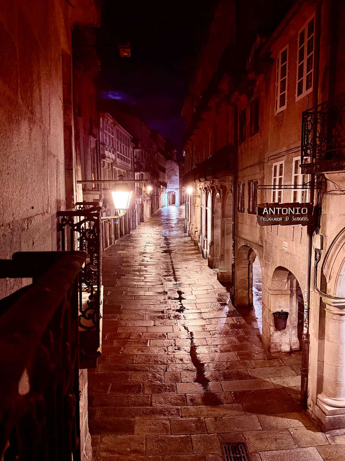 Nighttime view of a rain-slicked stone street illuminated by lanterns in Santiago de Compostela's Old Town.