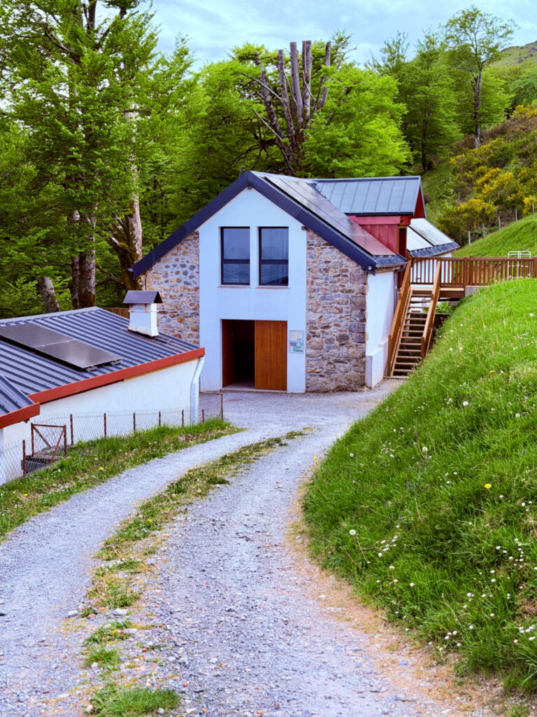 Albergue Borda in Honto, France, a modern stone-and-white building surrounded by green hills and trees along the Camino de Santiago.