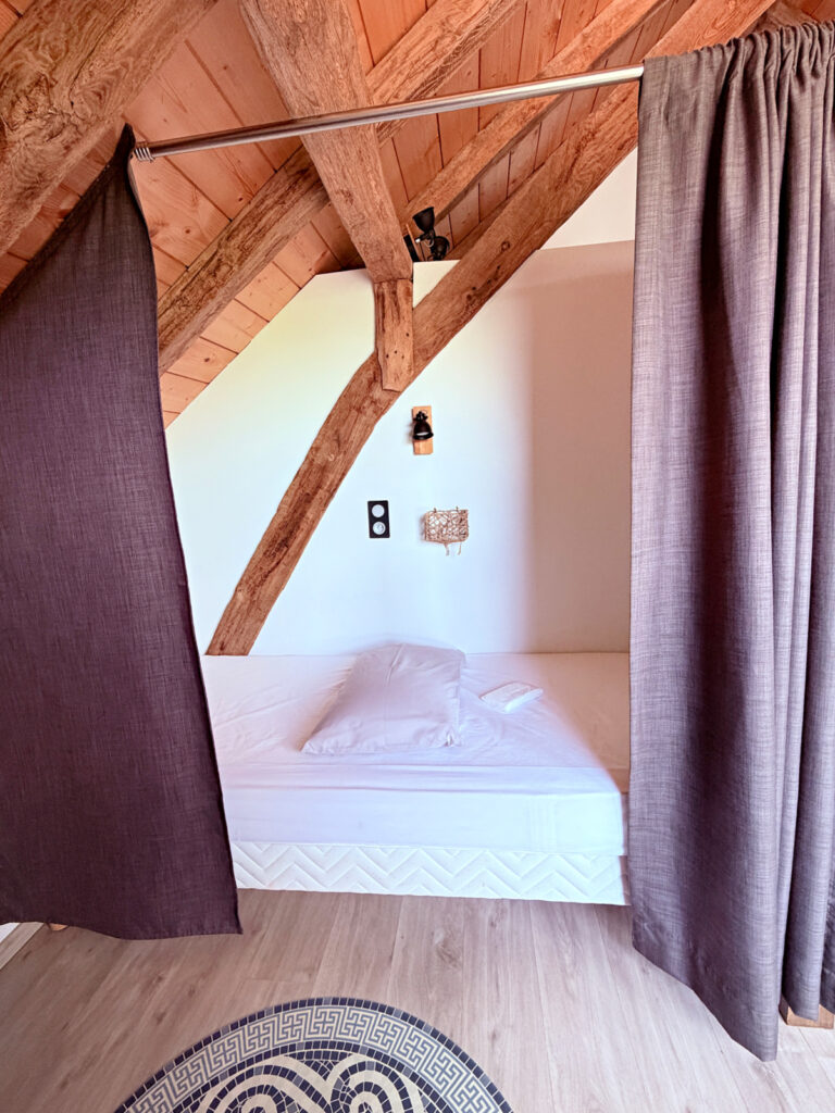 Private curtained sleeping space with a single bed and exposed wooden beams at Auberge Borda in Honto, France.
