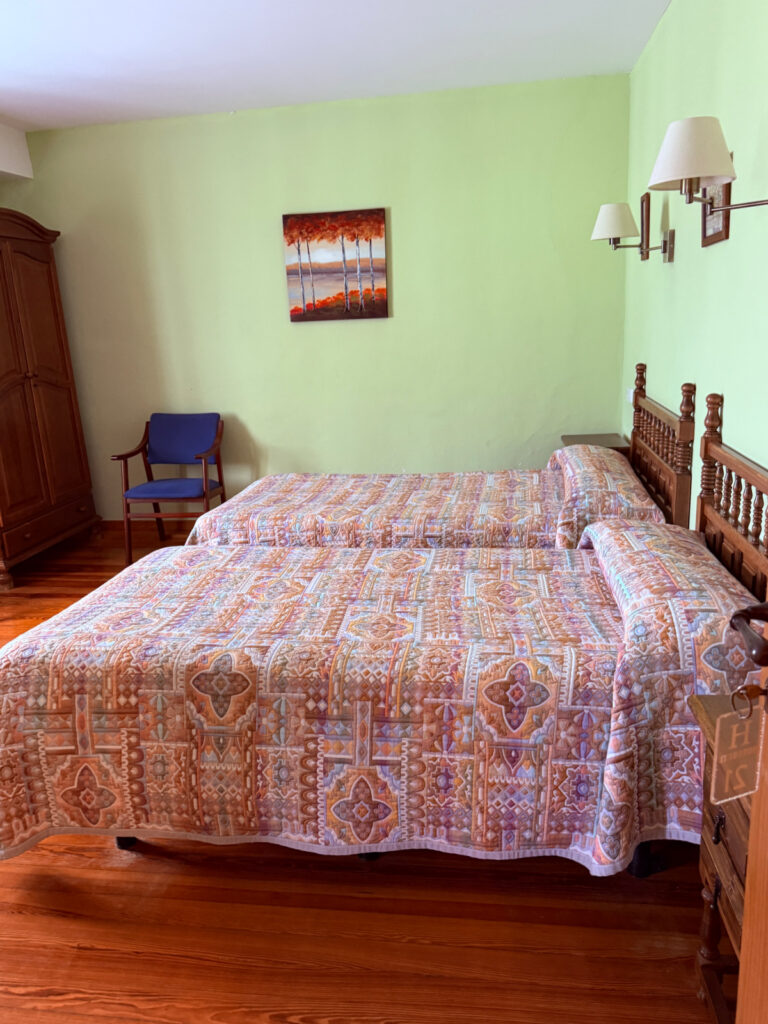 Simple room with two beds, wooden floors, and traditional furnishings in a hostal in Burguete, Spain.