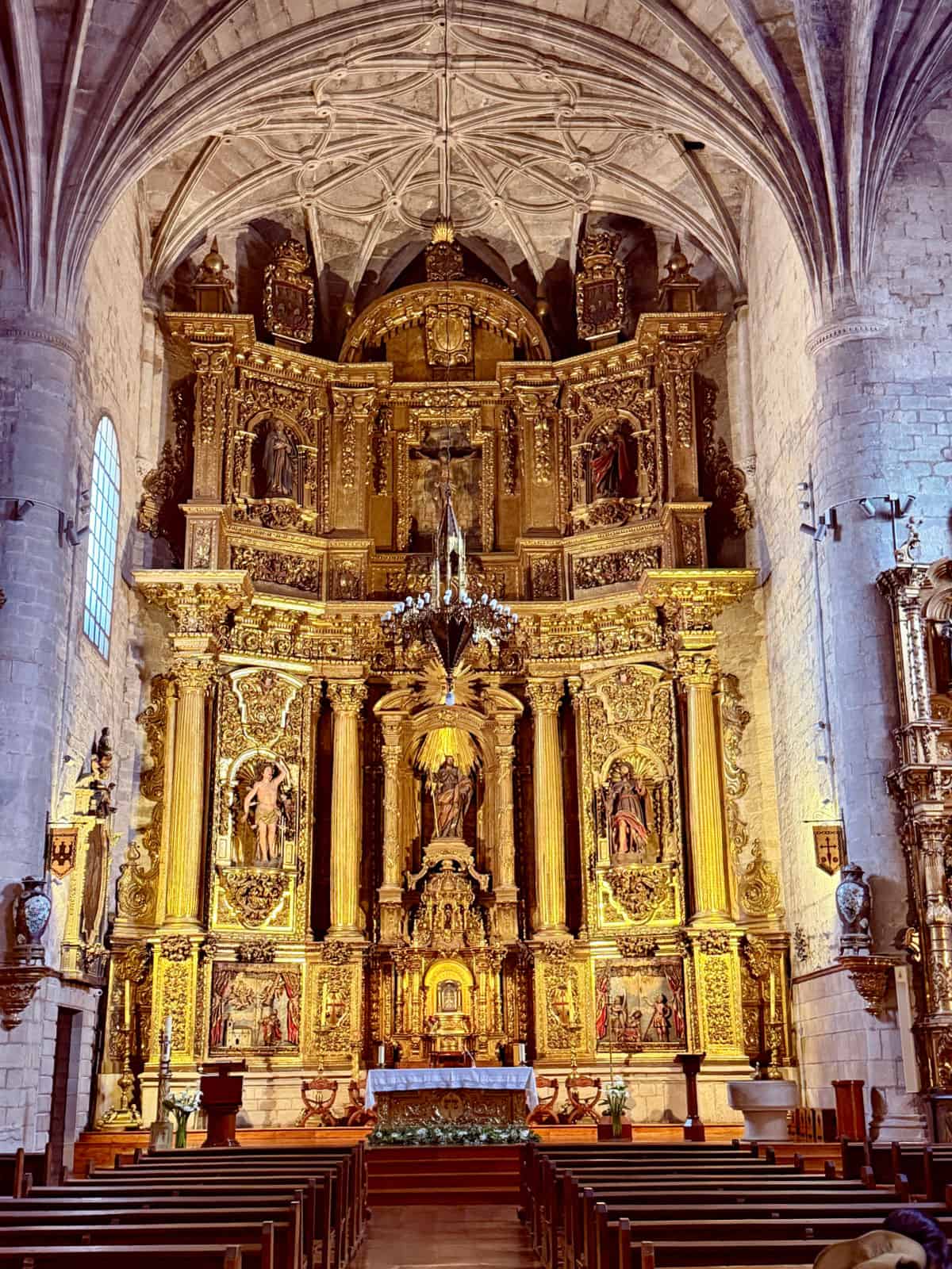 Ornate gilded altarpiece inside a historic Camino church, with vaulted stone ceilings, carved religious figures, and rows of wooden pews.