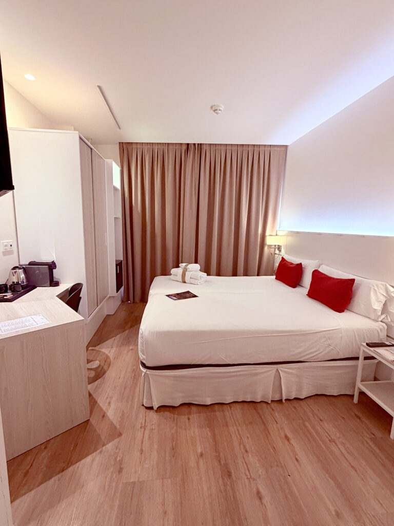 Comfortable hotel room in Pamplona with a double bed, desk, coffee maker, and floor-to-ceiling curtains.