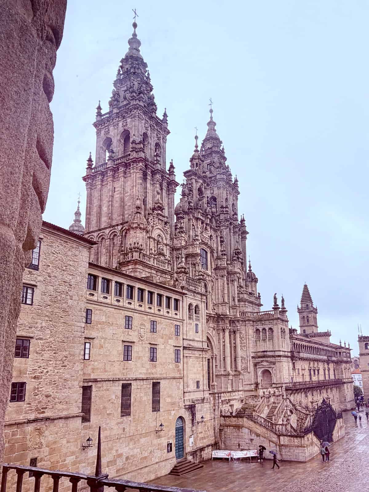 View of the ornate towers and stone façade of Santiago de Compostela Cathedral from the Parador de Santiago on a rainy day.