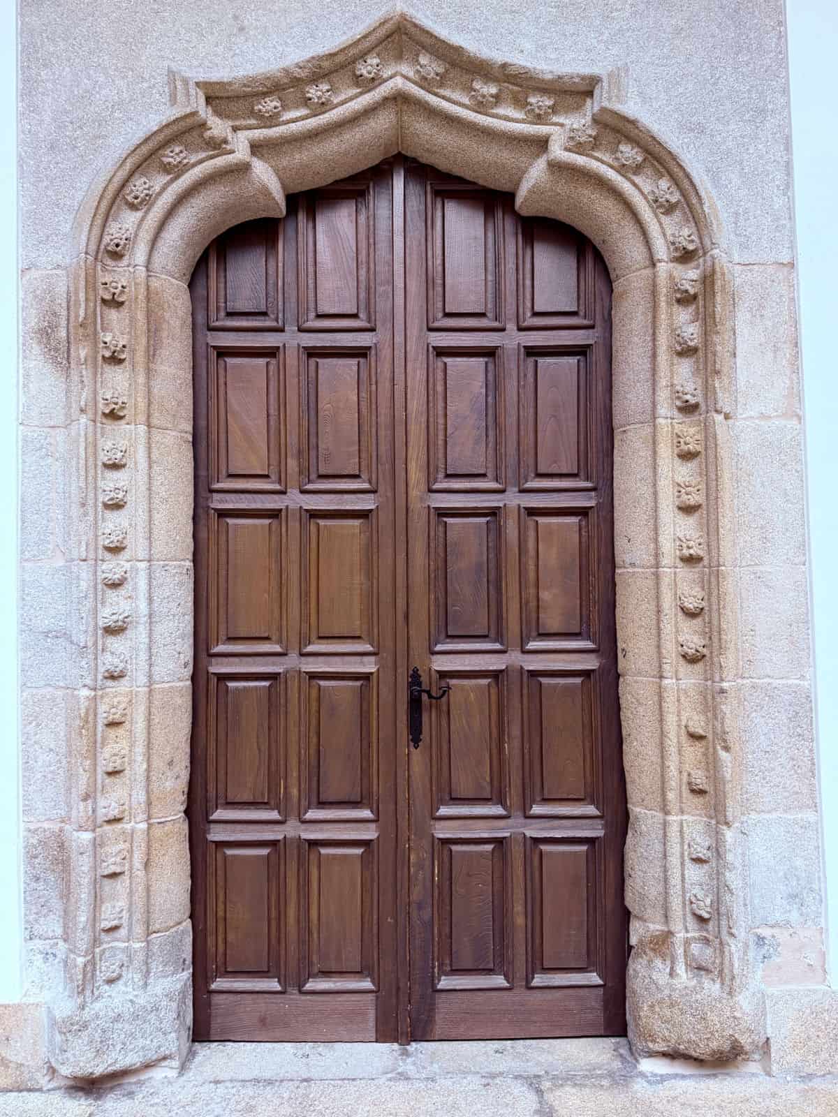 Ornately carved stone doorway with heavy wooden double doors inside the historic Parador de Santiago.