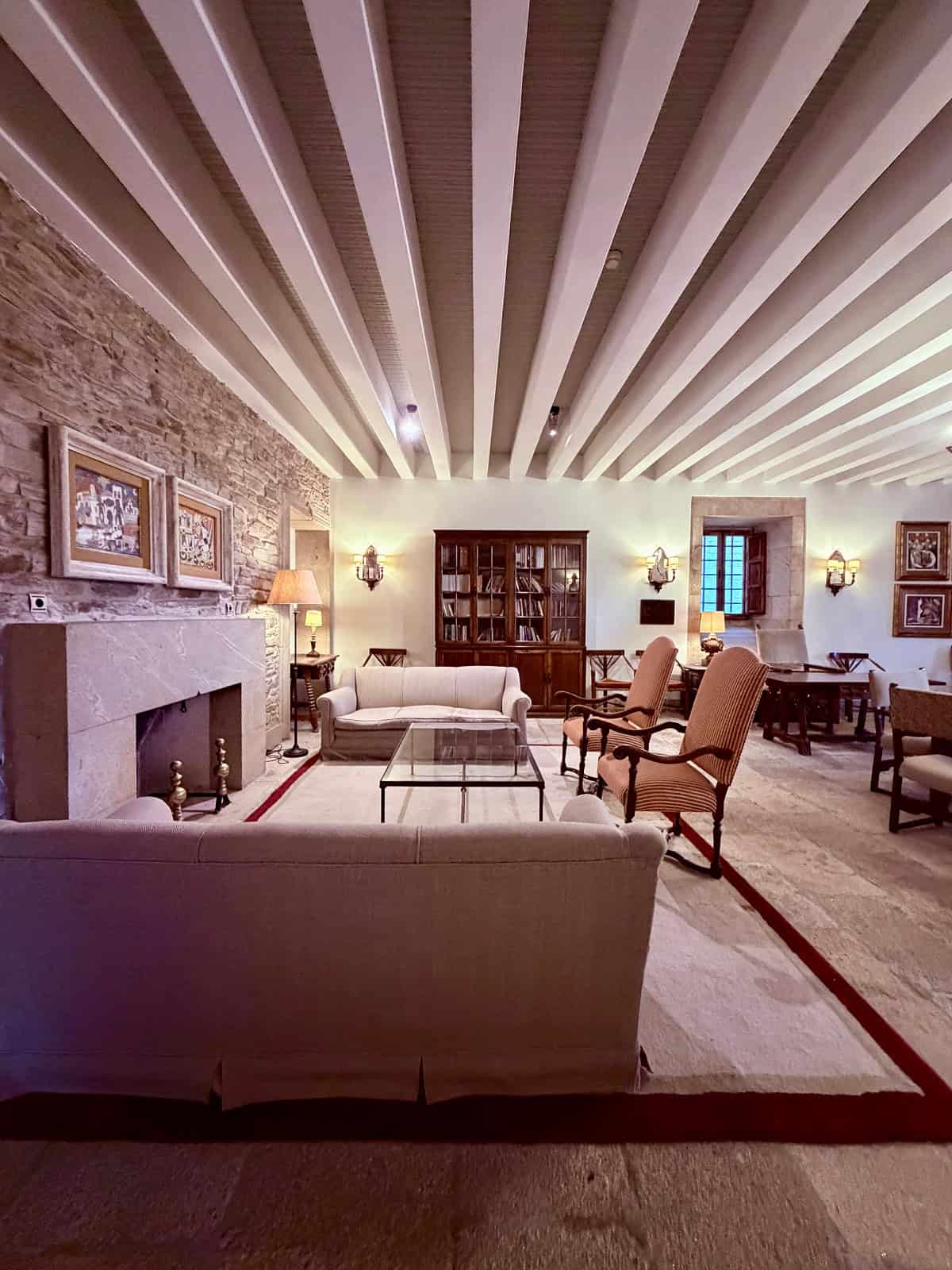 Elegant guest lounge at the Parador de Santiago with stone fireplace, comfortable seating, bookshelves, and historic architectural details.