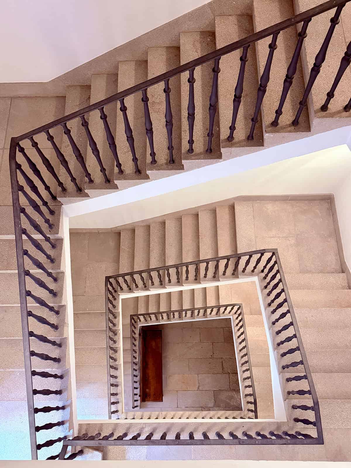 Geometric view looking down the multi-story stone stairwell at the Parador de Santiago de Compostela.