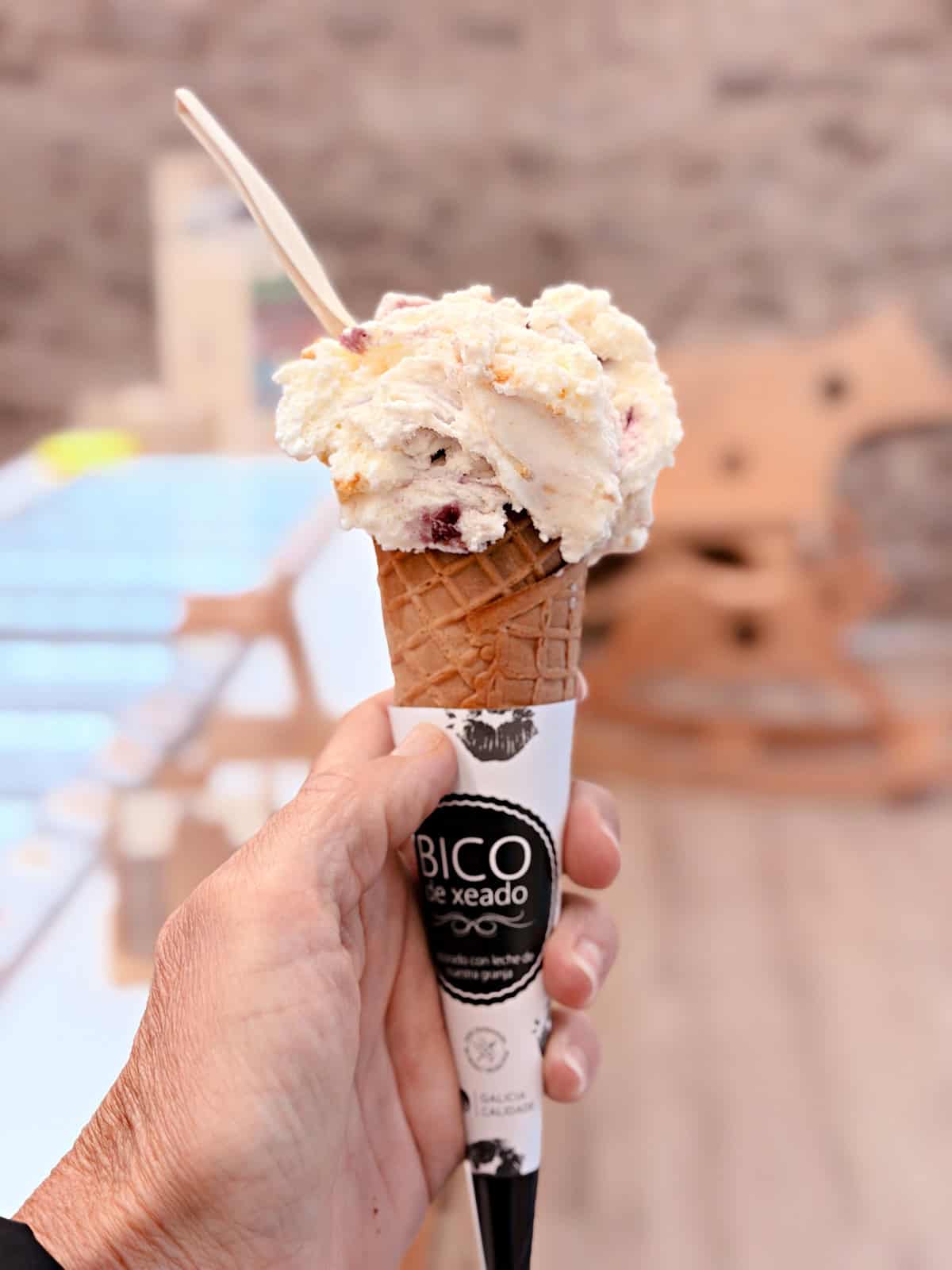 Hand holding a scoop of artisan ice cream in a waffle cone in Santiago de Compostela, Spain.