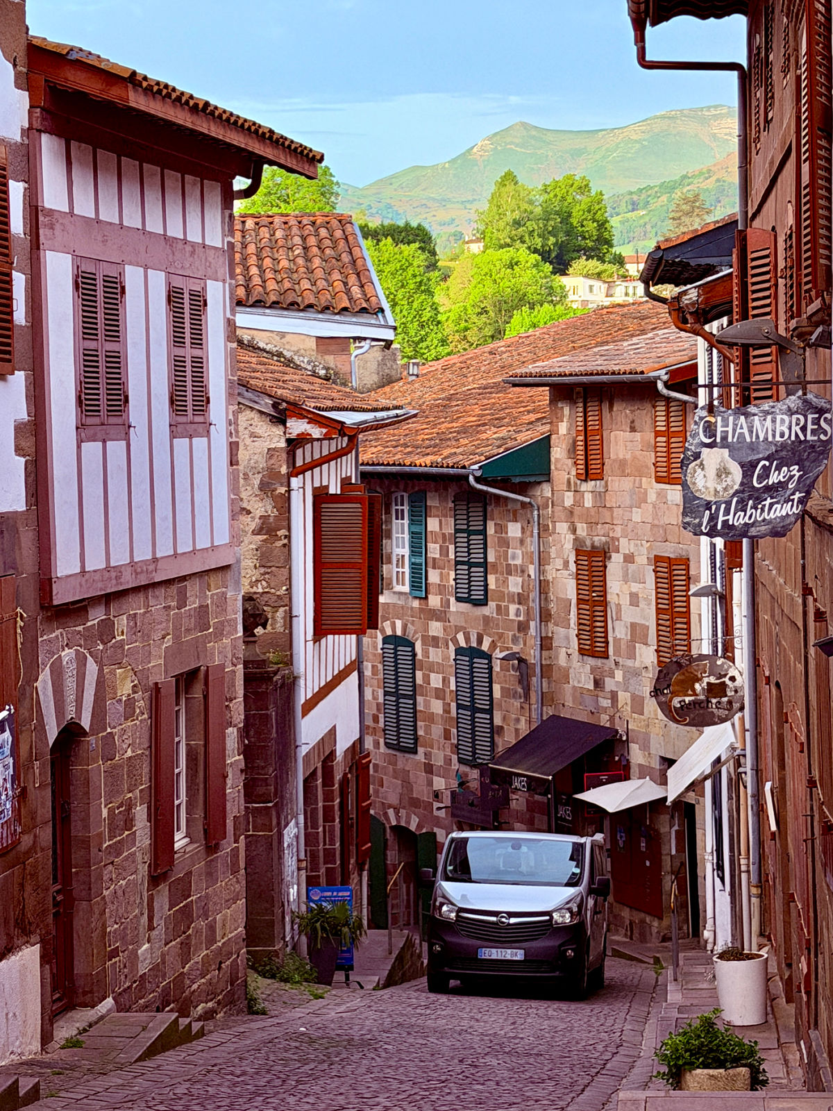 Charming cobblestone street in Saint-Jean-Pied-de-Port, France, framed by traditional Basque buildings and mountain views beyond the village.