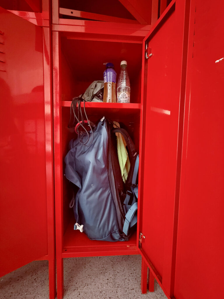 Red storage lockers holding a pilgrim backpack and gear at an albergue on the Camino de Santiago.