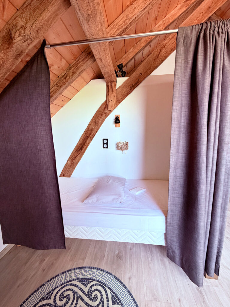 Private sleeping alcove with curtains, mattress, and exposed timber beams at Auberge Borda in Honto.