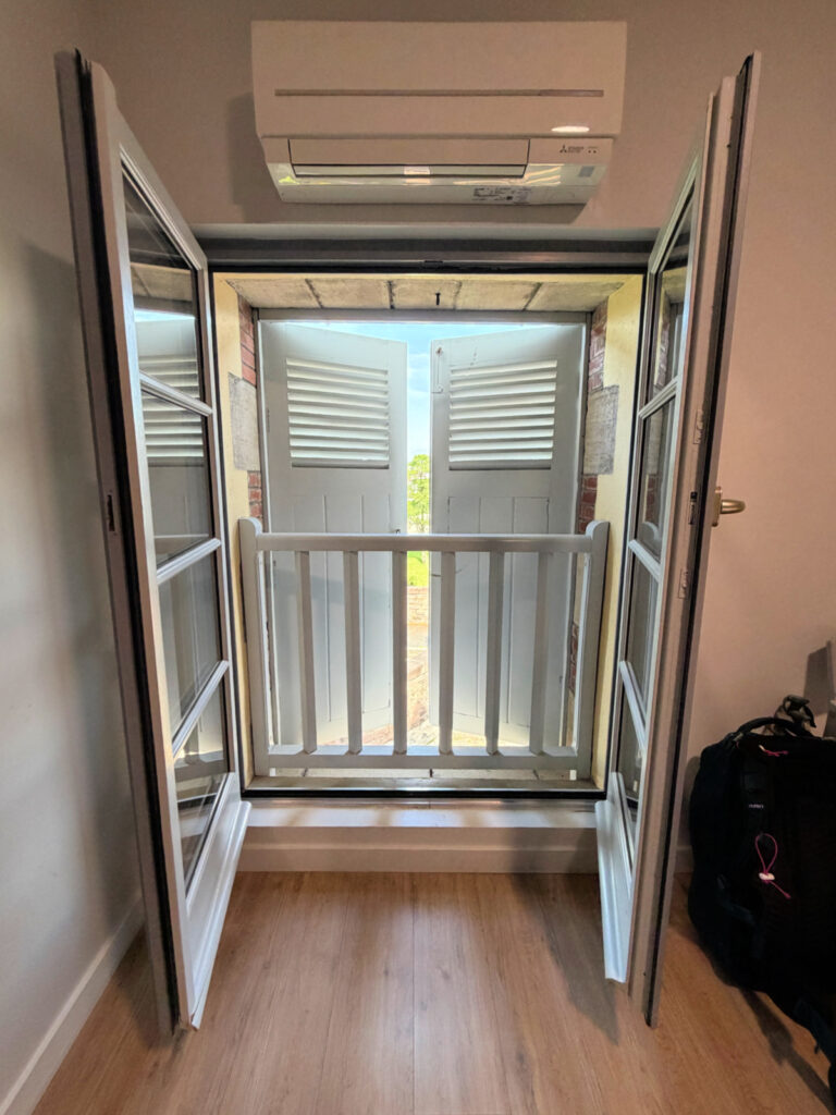 Traditional French shutters opened in a guest room at Hotel La Villa Esponda with air conditioner above and views outside.