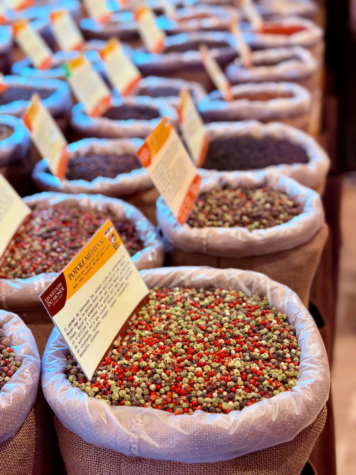 Open sacks filled with colorful peppercorns and spices for sale at a French market.