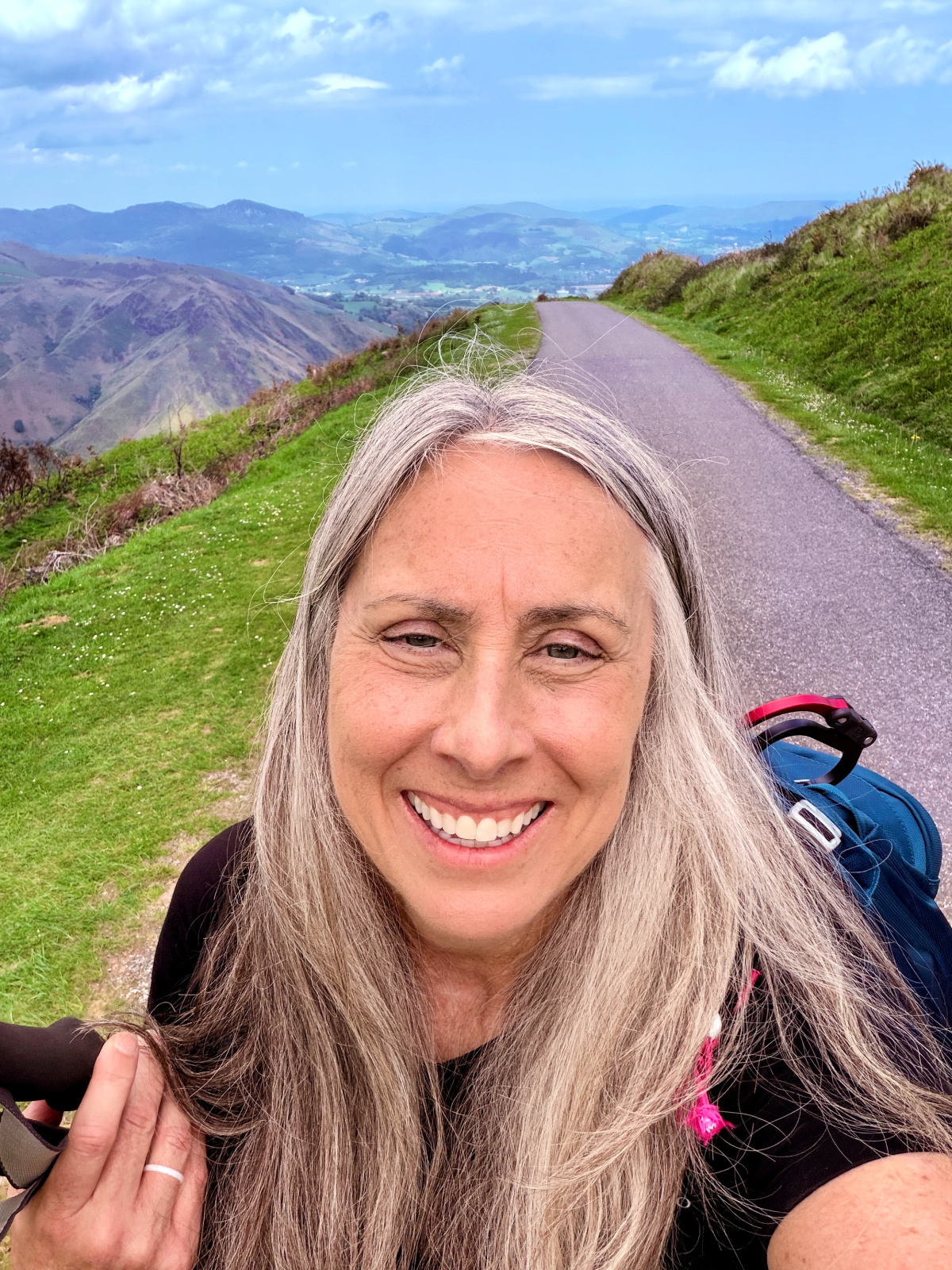 Smiling Camino pilgrim carrying a backpack on a mountain road in the French Pyrenees.