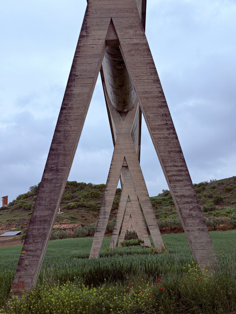 Tall triangular stone aqueduct supports rising above the green countryside along the Camino Francés.