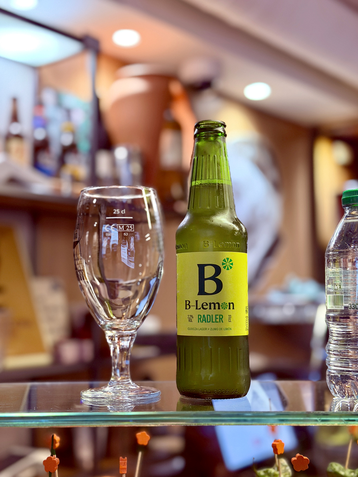 Bottle of B Lemon Radler beside an empty glass at a bar in Spain.