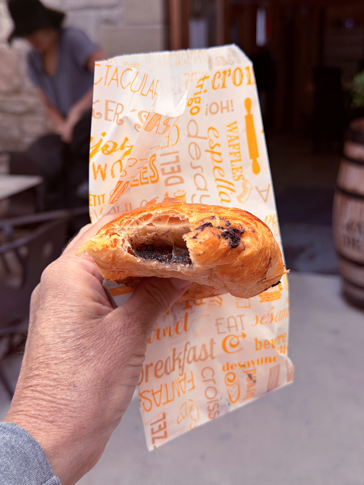 Hand holding a chocolate-filled pastry wrapped in printed paper.