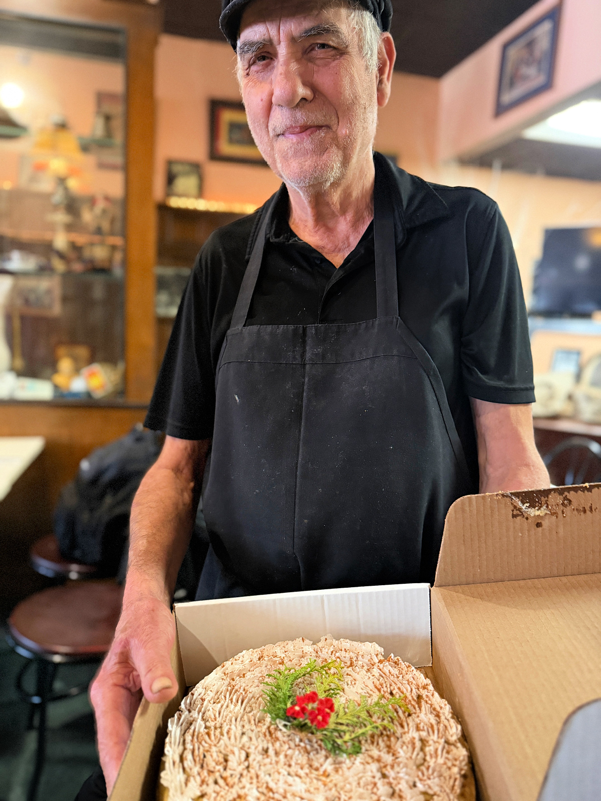 Christos, owner of Christos Mediterranean Grille in downtown Pittsburgh, holding his Jackie O cake, topped with whipped cream, cinnamon, and a sprig of greenery.