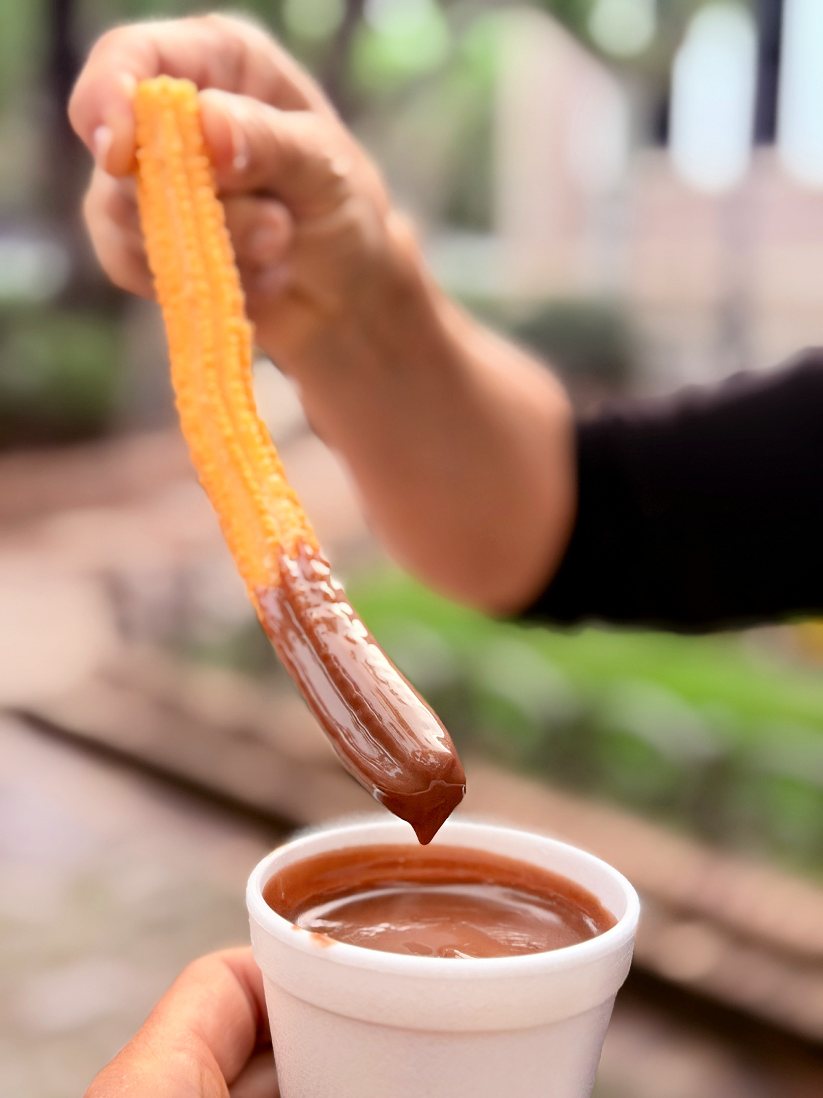 Fresh churro being dipped into a cup of thick hot chocolate.