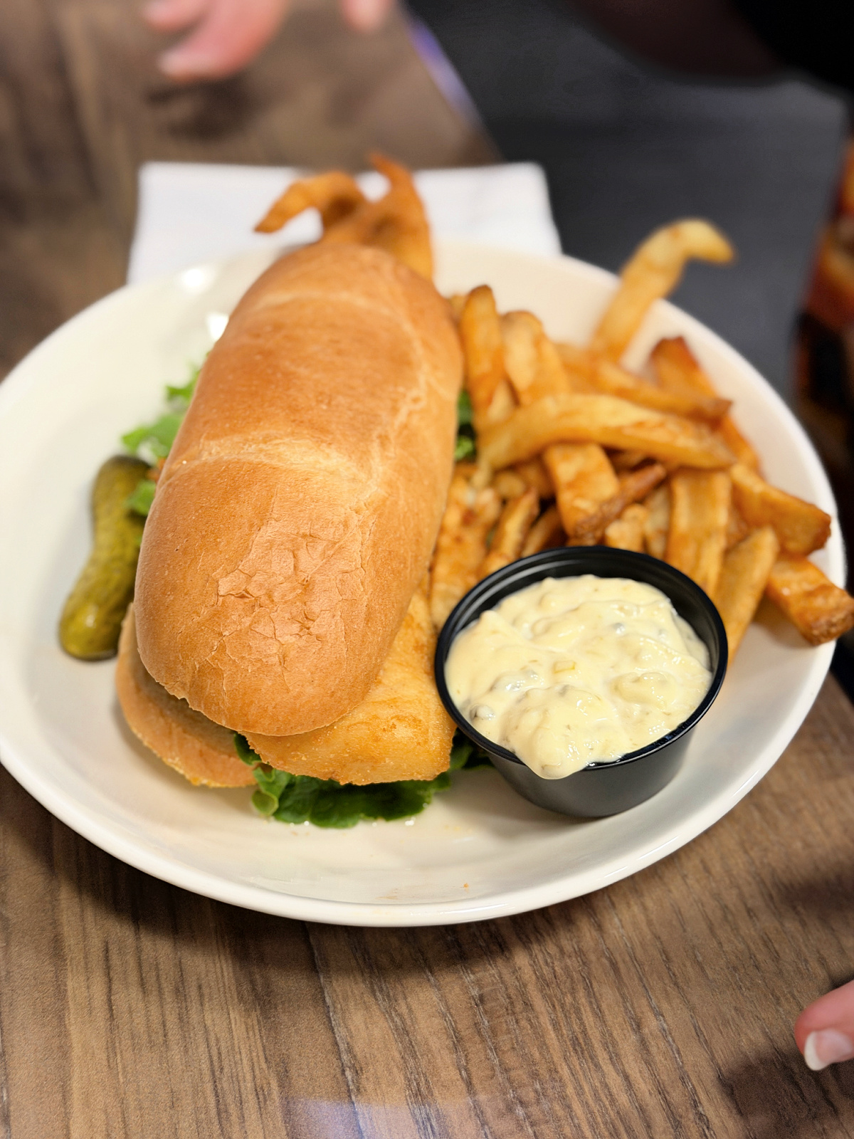 Colossal Fish Sandwich with a fried fish fillet hanging out of a hoagie roll, served with French fries, a pickle spear, and tartar sauce at the Wheelhouse in Pittsburgh.
