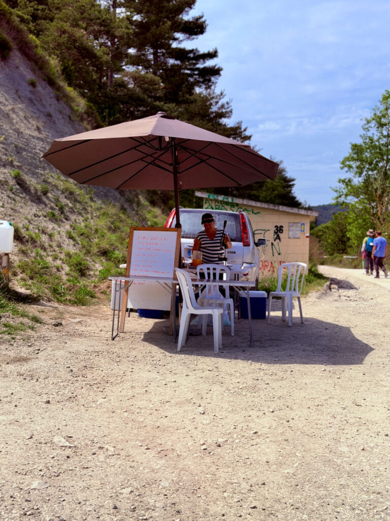 Roadside drink stand offering refreshments to Camino pilgrims along a gravel trail in Spain.