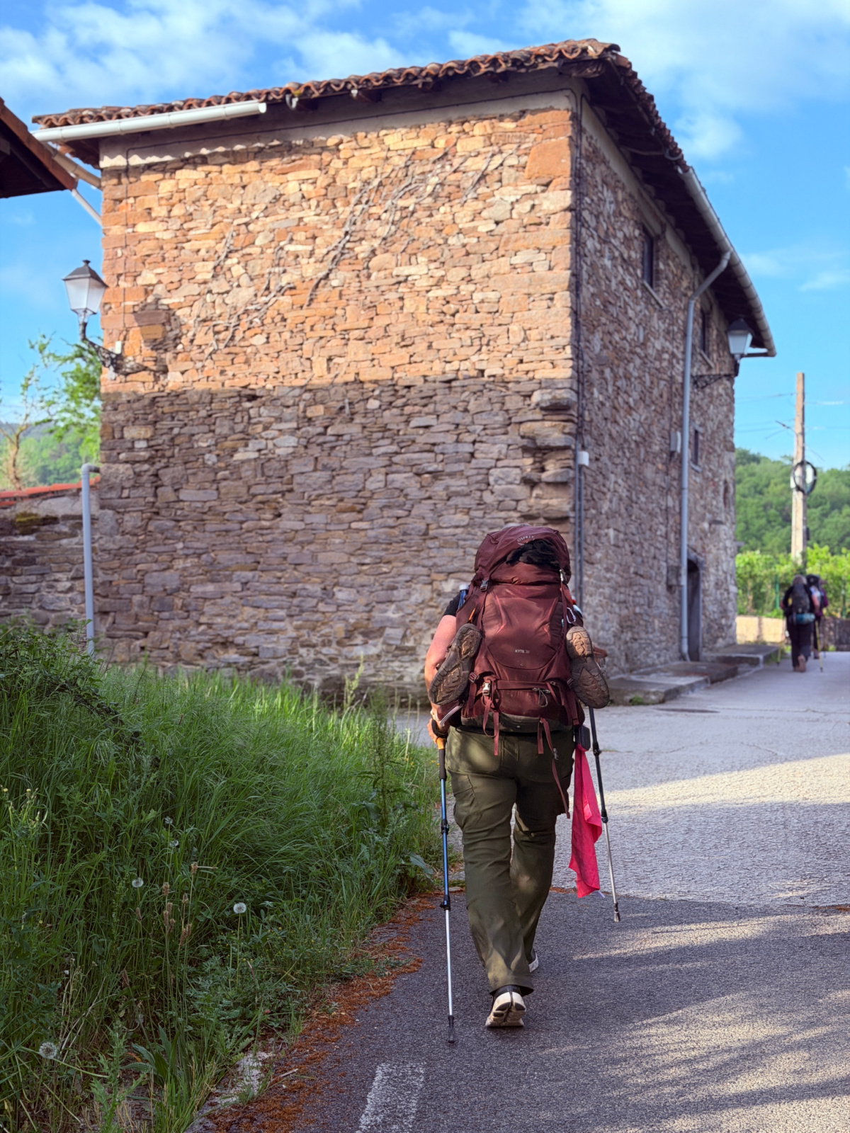 Backpacking pilgrim walks past an old stone building along the Camino de Santiago in Spain.